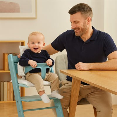 Un bébé qui est assis sur une chaise haute à côté de son père sur le coussin