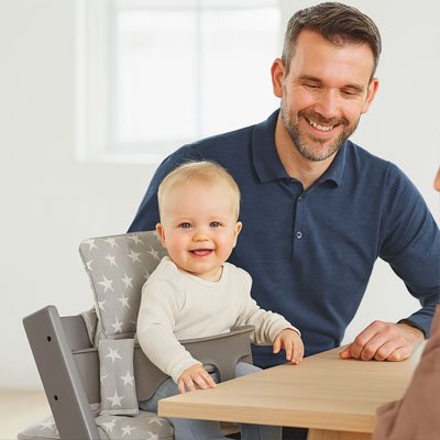 Un bébé qui est assis sur une chaise haute à côté de son père sur le coussin