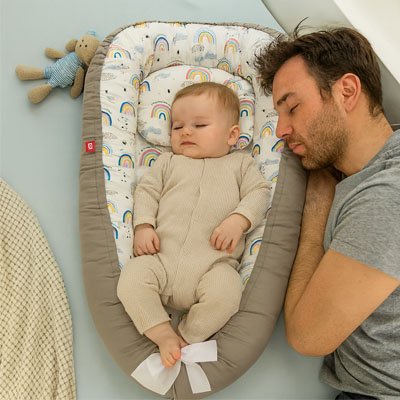 Un bébé qui dort dans un réducteur de lit pour bébé avec son père à côté.
