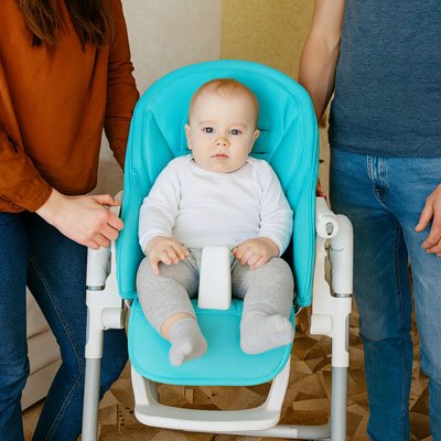 Un bébé qui est assis sur un cousin chaise haute, son père et sa mère sont à côté 