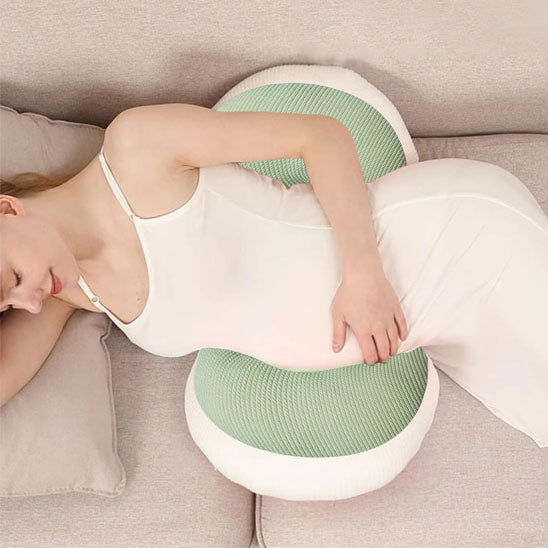 maman enceinte couchée sur le côté et appuyée sur un coussin grossesse vert